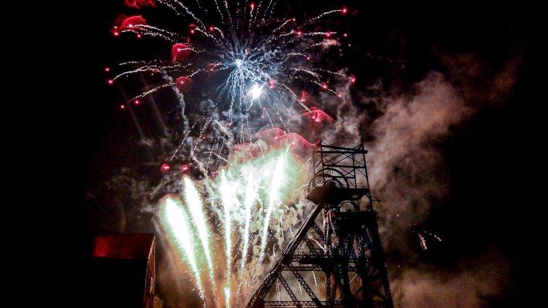 Illuminated fireworks display above a dramatic industrial structure